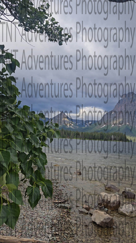 Lake with mountains in the background under a cloudy sky, viewed through tree branches